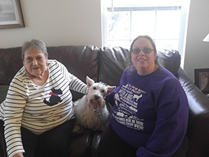 A friendly visitor sitting on a couch with a senior and her small dog
