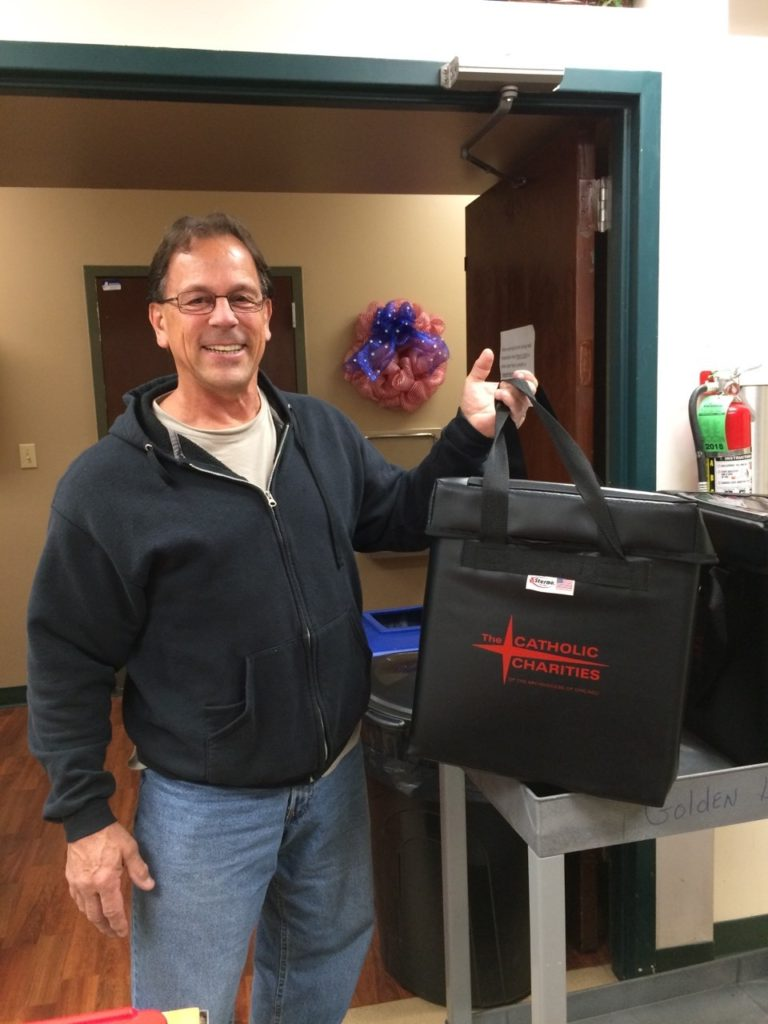 Stan, an AmeriCorps Seniors volunteer, holding a Catholic Charities meal delivery bag